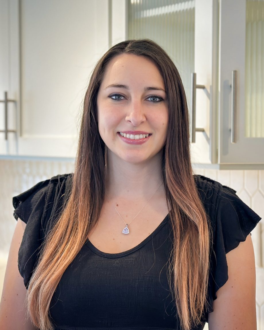 Professional headshot of an S&A Homes team member smiling in a model home kitchen with white cabinets in the background.