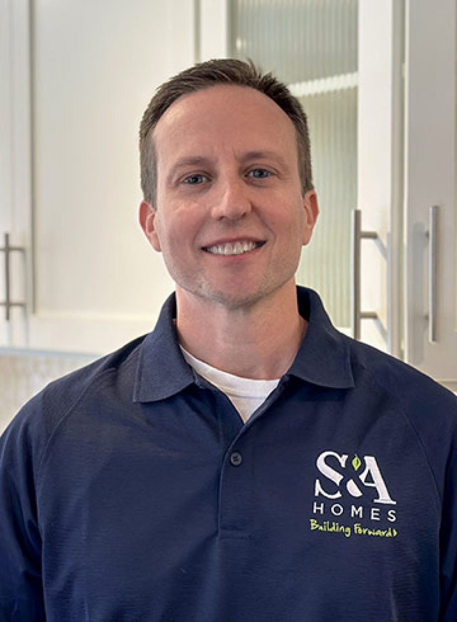 Professional headshot of an S&A Homes team member wearing an S&A Homes polo shirt, smiling in a model home kitchen.