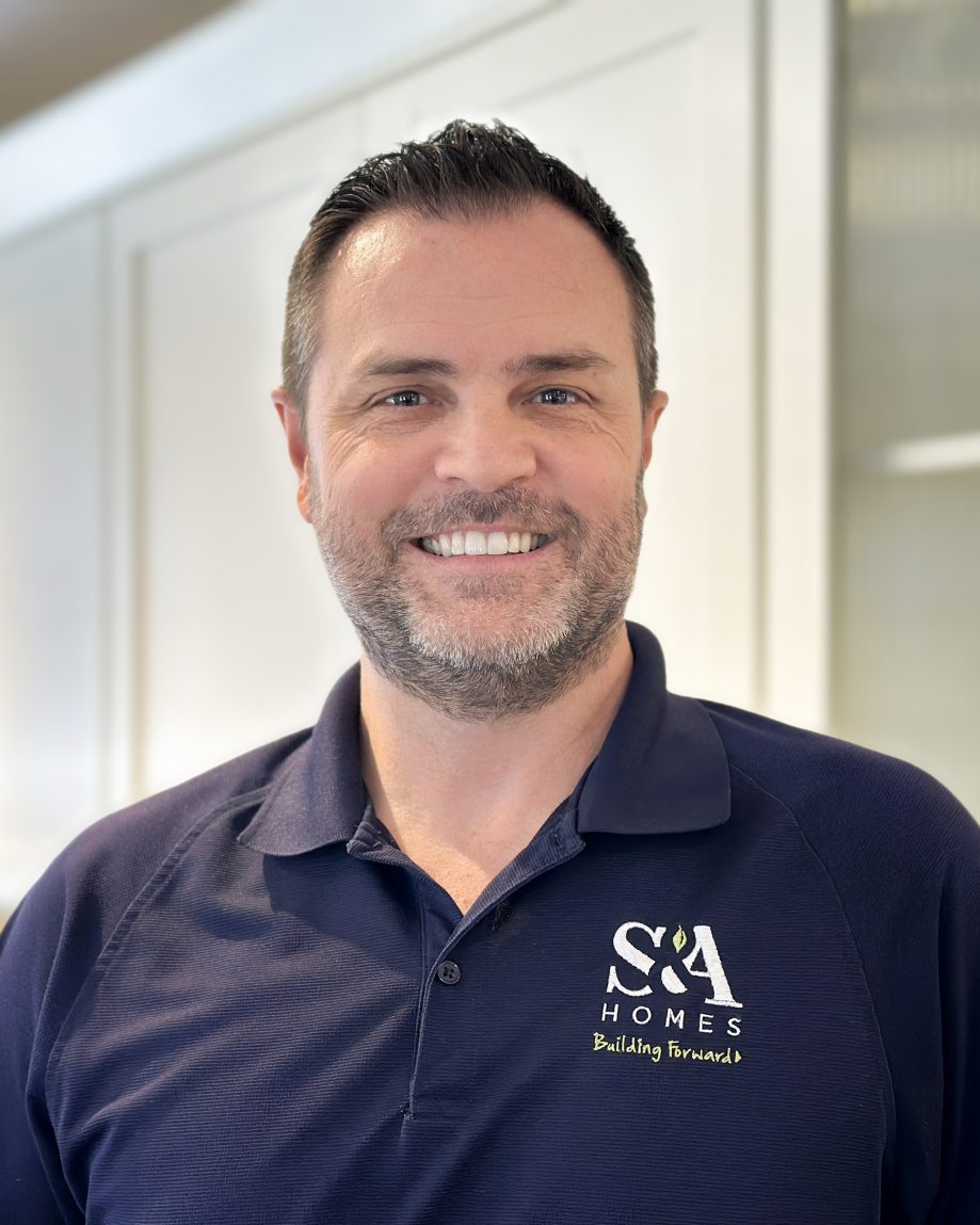 Professional headshot of an S&A Homes team member wearing an S&A Homes polo shirt, smiling in a model home kitchen.