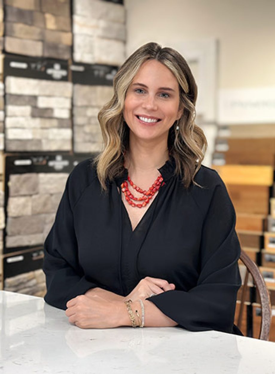 Professional headshot of an S&A Homes team member smiling in a design center with cabinetry and finish samples in the background.