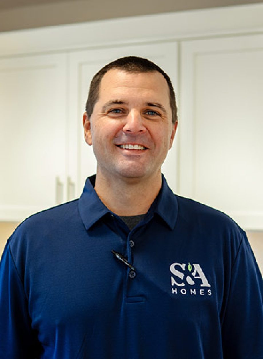 Professional headshot of an S&A Homes team member wearing an S&A Homes polo shirt, smiling in a model home kitchen.