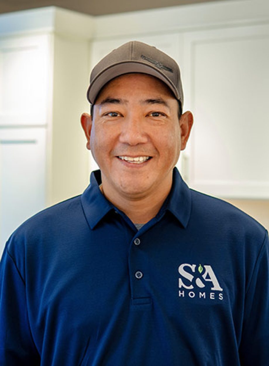 Professional headshot of an S&A Homes team member wearing an S&A Homes polo shirt, smiling in a model home kitchen.