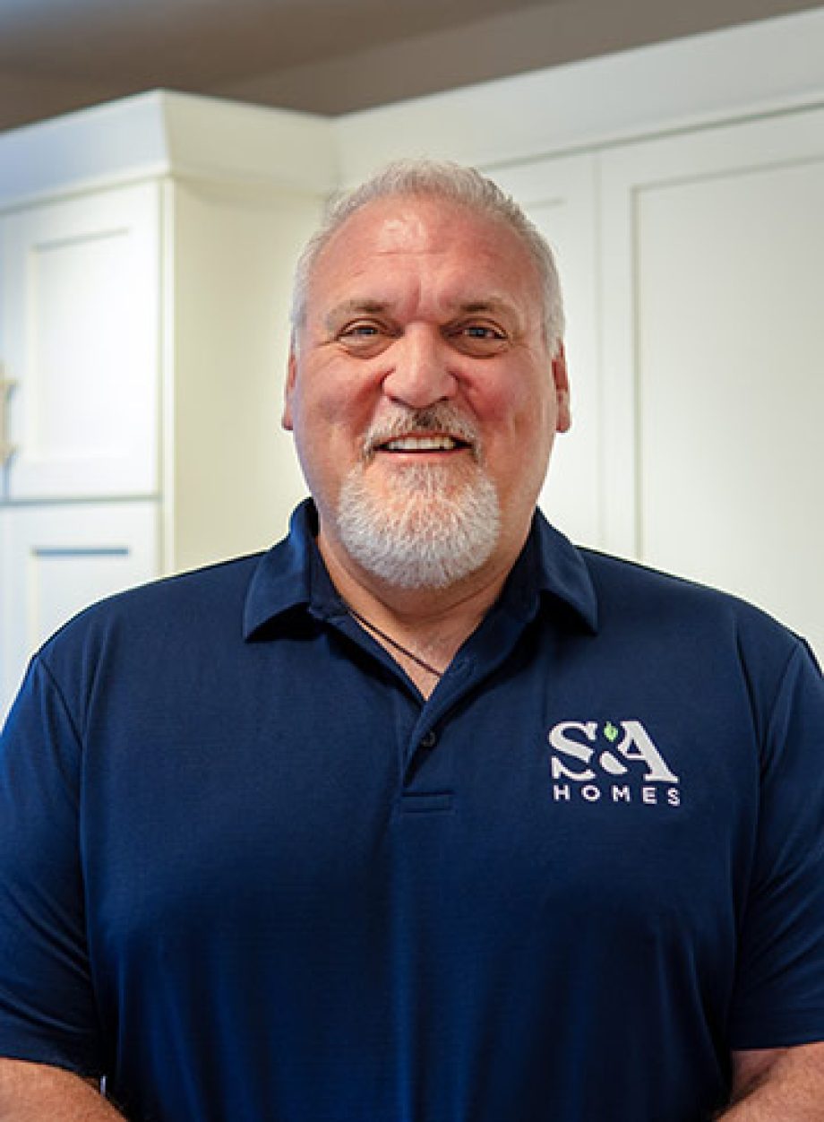 Professional headshot of an S&A Homes team member wearing an S&A Homes polo shirt, smiling in a model home kitchen.