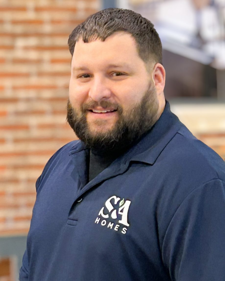 Professional headshot of an S&A Homes team member wearing an S&A Homes polo shirt, smiling in front of a brick backdrop.