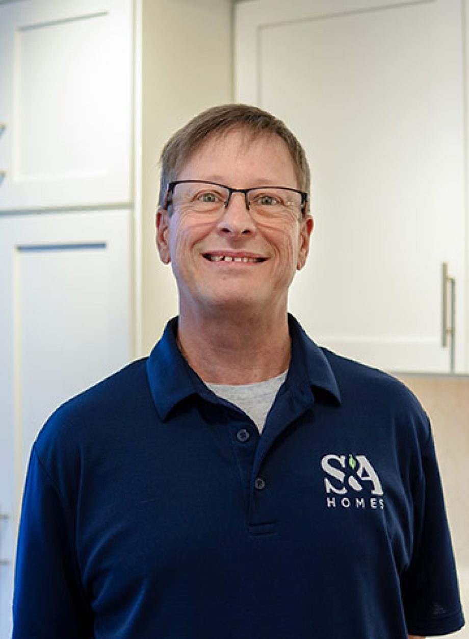 Professional headshot of an S&A Homes team member wearing an S&A Homes polo shirt, smiling in a model home kitchen.