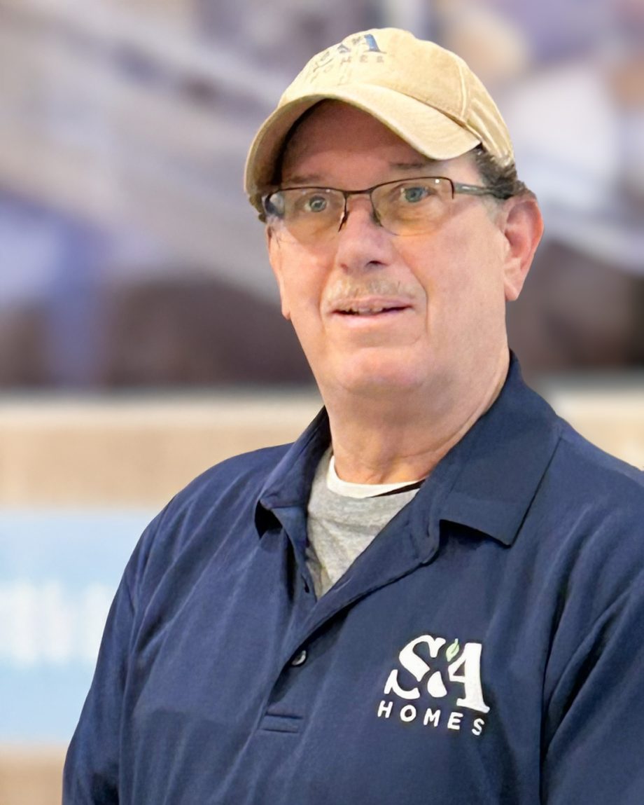 Professional headshot of an S&A Homes team member wearing an S&A Homes polo shirt and baseball cap, smiling indoors.
