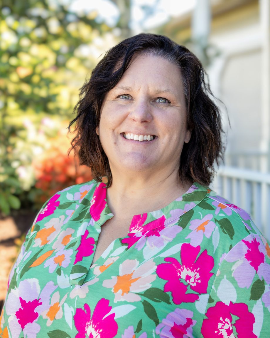 Professional headshot of an S&A Homes team member wearing a floral shirt and smiling outdoors with trees in the background.